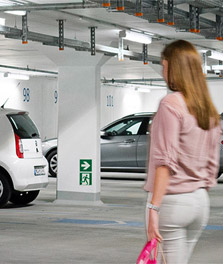 Une femme se dirige vers sa voiture dans un parking GreenParking. – éclairage pour le commerce