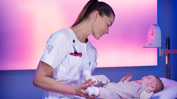 Une infirmière pèse un bébé dans une chambre délicatement éclairée – éclairage des établissements de santé
