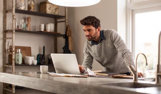 Un homme utilise un ordinateur portable dans un bureau à domicile bien éclairé avec un éclairage d'appoint à LED pour une configuration de travail à distance efficace.